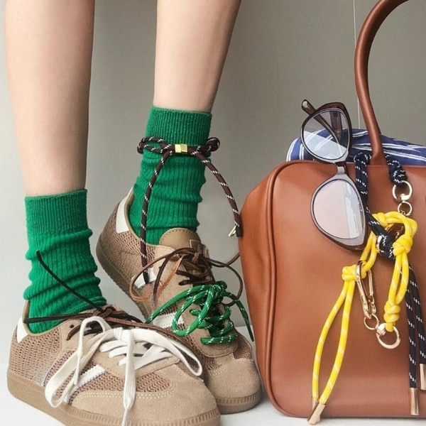 A close-up product hero shot featuring suede sneakers, bright green socks, and a coordinated leather bag to establish a cohesive lifestyle aesthetic.