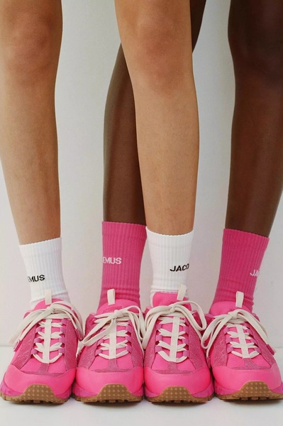 A minimalist, low-angle product shot of four pairs of legs wearing matching socks and bright pink running shoes, focusing on product uniformity.