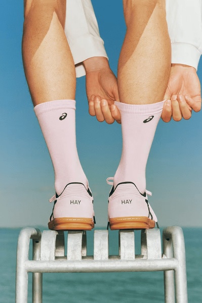 A close-up, rear-view shot of a person adjusting their socks while wearing branded running shoes on a high-mounted metal structure against a clear sky.