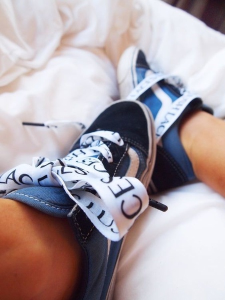 A close-up personal perspective of a pair of sneakers on a bed, utilizing customized branded laces to create a unique and intimate visual hook.