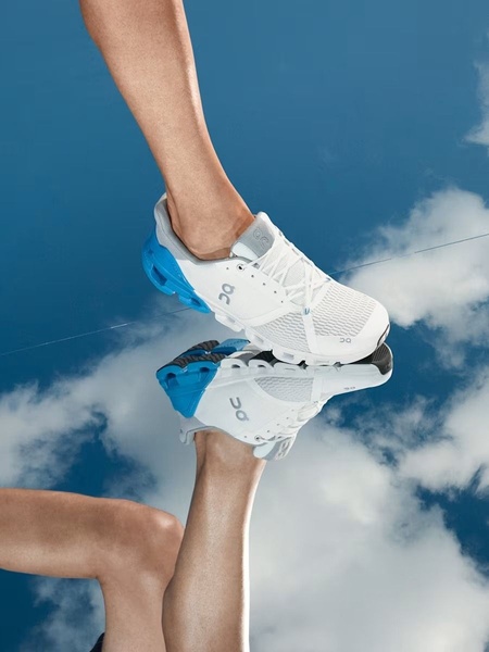 A high-contrast 3:4 vertical shot showing a running shoe against a bright blue sky, utilizing a mirrored reflection to create an illusion of weightlessness.