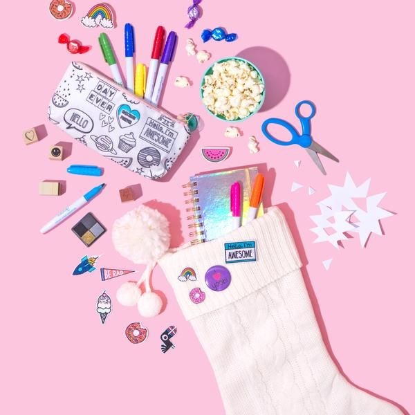 A high-angle flat lay composition featuring stationery, pens, and a stocking on a soft pink background to highlight giftability.