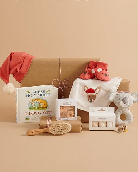 A well-organized flat lay photography shot showcasing a baby gift set including a book, baby booties, a koala rattle, and branded clothing.