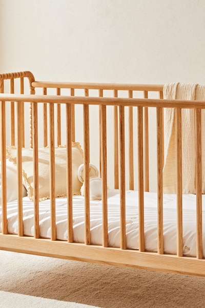 A minimalist, high-quality product hero shot of a wooden crib featuring soft linens, natural lighting, and a serene nursery atmosphere.