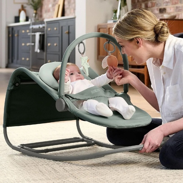 A high-quality lifestyle shot capturing a mother interacting with her infant in a modern, neutral-toned baby bouncer within a home setting.
