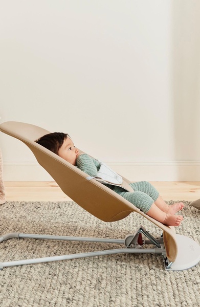 A high-quality, studio-lit photograph of a baby sitting in a modern, neutral-toned bouncer on a textured rug, emphasizing design and comfort.