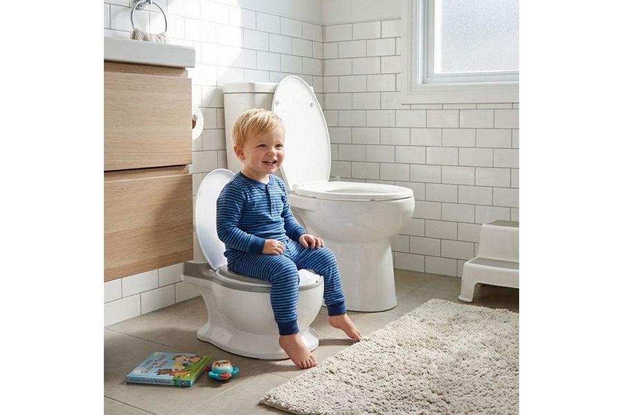 A high-trust lifestyle image featuring a toddler confidently sitting on a training potty in a clean, brightly lit home bathroom.