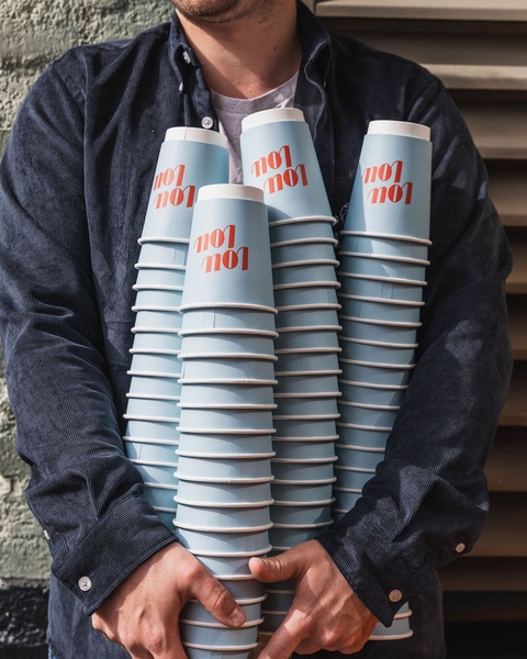 A close-up shot of a person holding a large stack of branded paper coffee cups, emphasizing the abundance and professional supply of the product.
