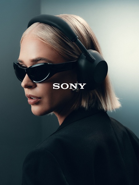 A high-fashion portrait of a model wearing premium wireless headphones in a monochromatic, studio-lit environment.