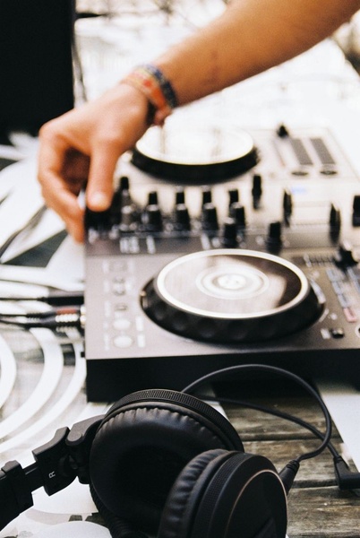 A close-up, high-angle shot focusing on the hands of a DJ manipulating a professional audio controller, framed by studio headphones in the foreground.