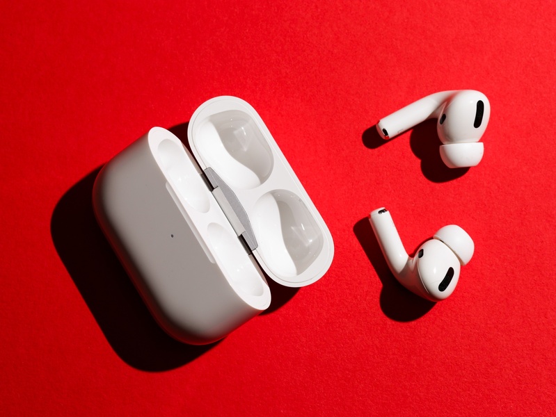 A high-contrast, minimalist studio product shot featuring wireless earbuds and their charging case against a bold red background.