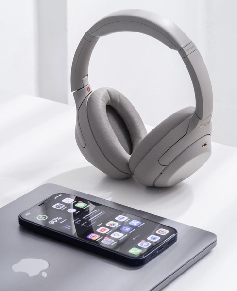 A high-end, clean product shot of headphones positioned next to a smartphone on a laptop, emphasizing a premium and organized workspace aesthetic.
