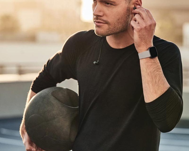 A close-up, high-contrast lifestyle shot of a man wearing a sleek smartwatch while holding a medicine ball, emphasizing fitness and professional style.