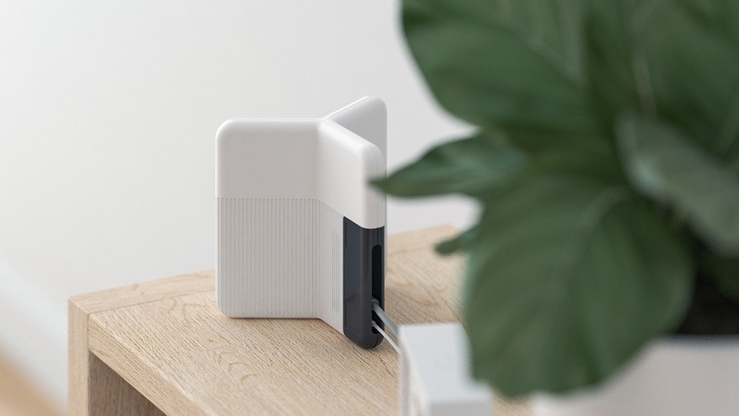 A clean, high-angle product photograph of a modern white cable organizer sitting on a light wood surface next to a green plant.