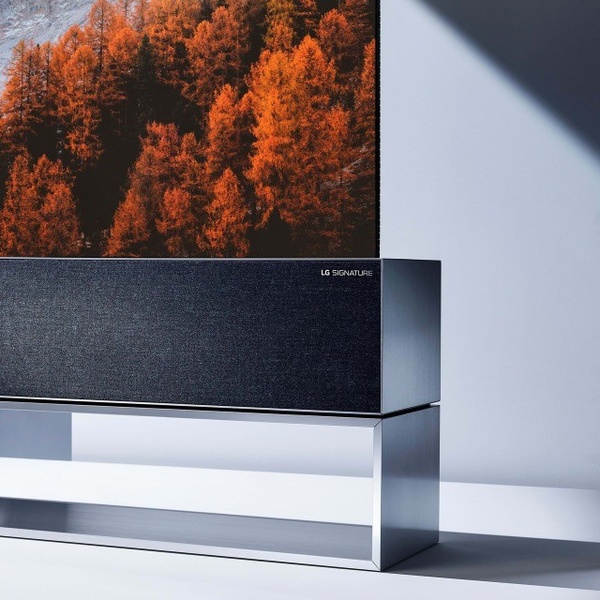 A high-end visual composition featuring a premium rollable TV displaying a vibrant autumn forest scene against a clean, architectural background.