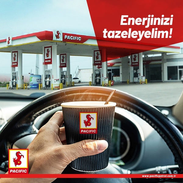 A high-contrast 1:1 image showing a first-person perspective of holding a branded paper coffee cup while parked at a petrol station.