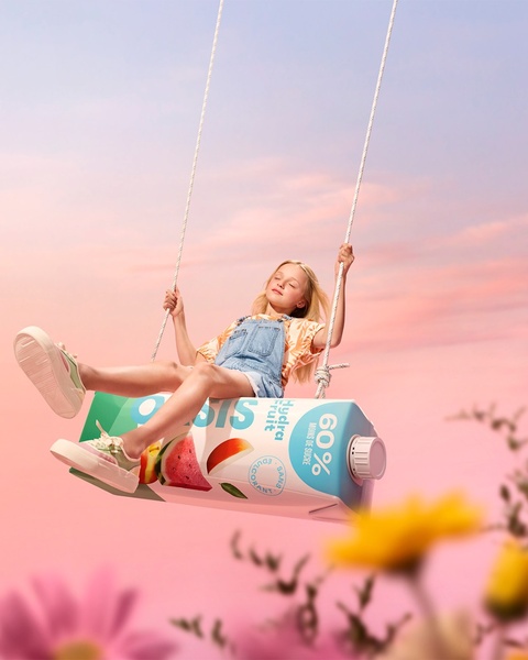 A young girl is shown swinging on a giant juice carton against a dreamy sunset, highlighting the drink's natural fruit ingredients and low sugar content.
