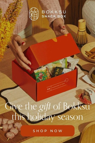 A close-up, warm-toned image showing a person opening a red subscription snack box, emphasizing the gift-giving experience for the holiday season.