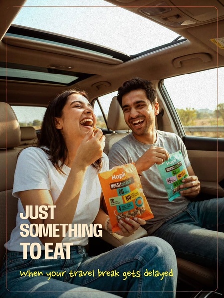 A high-quality candid shot of two people in a car laughing while holding bags of Muesli, illustrating a convenient snack choice for travel.