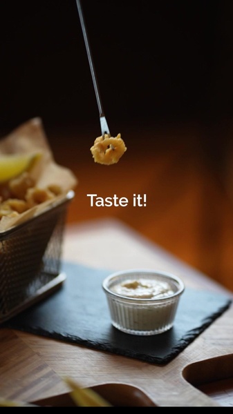 A close-up vertical shot showing a single piece of fried calamari being held by a fork above a side of dipping sauce to induce appetite appeal.