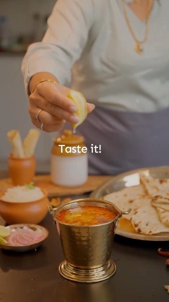 This ad creative utilizes a close-up, high-sensory action shot of a hand squeezing a lemon over a traditional Indian curry bowl to immediately capture viewer attention.