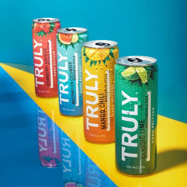 A clean, eye-level studio shot of four canned beverages arranged in a diagonal line against a dual-tone background.