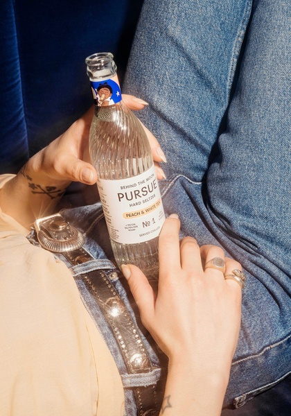 A close-up, natural light shot of a hard seltzer bottle held in a lap, showcasing a relaxed and approachable brand vibe.