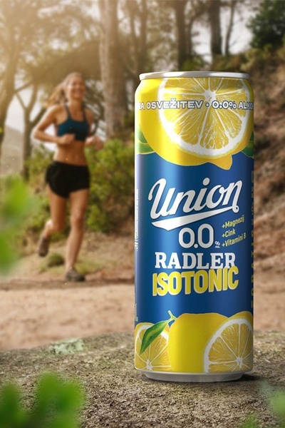 A high-quality product shot of an isotonic drink can placed in a natural outdoor setting, featuring a blurred runner in the background to suggest an active lifestyle.