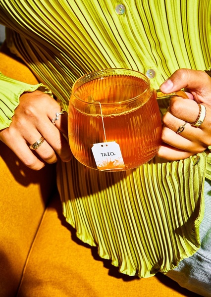 A close-up of a person holding a clear glass mug of tea, emphasizing a warm and inviting lifestyle atmosphere.