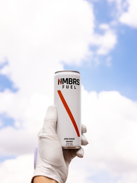 A high-contrast handheld shot of an orange energy drink can against a bright, cloudy blue sky, emphasizing brand clarity.