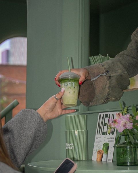 A close-up, high-quality shot of an iced matcha latte being handed over in a minimalist, aesthetically pleasing cafe environment.