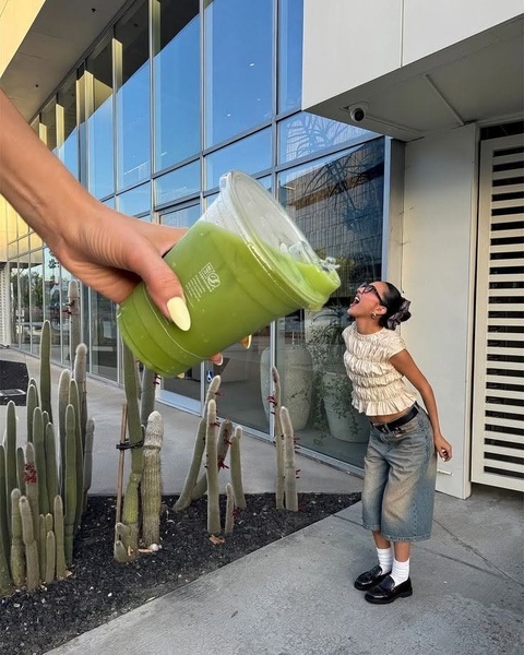 A creative visual of a human-sized hand pouring a regular-sized matcha drink toward a smaller-scale person, creating a surreal perspective effect.