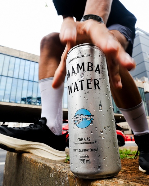 A high-energy, active shot featuring a hand reaching for a chilled can of sparkling mineral water in an urban outdoor setting.