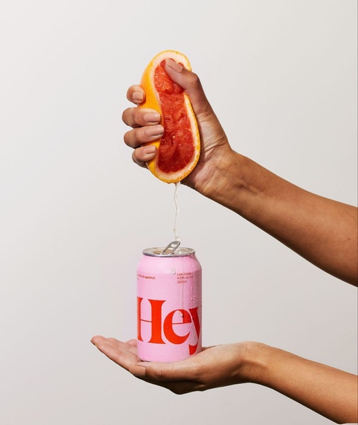 A close-up shot showing a hand squeezing a fresh grapefruit half directly into a chilled can of seltzer, highlighting raw, natural ingredients.