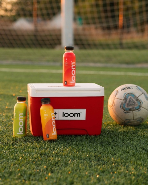 A clean, outdoor lifestyle shot featuring energy drink bottles arranged around a cooler on a soccer field at golden hour.