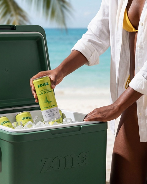 A lifestyle-focused shot showing a person reaching into a filled cooler for a chilled can of hard seltzer on a sunny beach.