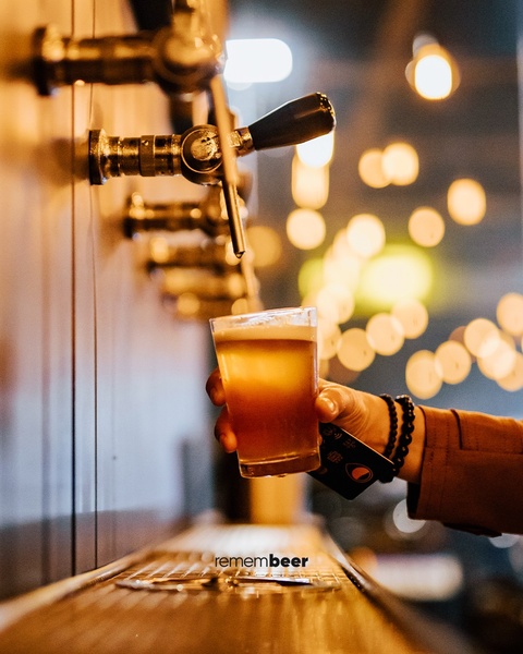 A close-up shot capturing a fresh beer being poured from a tap handle, featuring warm ambient bokeh lighting to emphasize product quality.