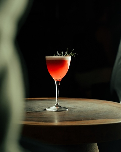 A high-contrast, moody photograph of a single craft cocktail garnished with a sprig of rosemary on a wooden table, emphasizing premium quality and sophistication.