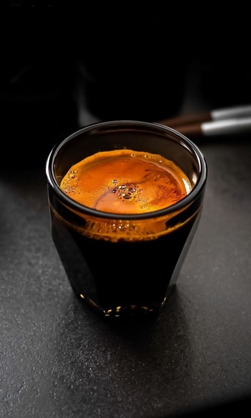 A high-contrast, macro-style close-up of a fresh espresso shot in a glass cup, focusing on the rich crema and deep textures.