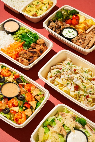 A high-angle, top-down shot showing a variety of healthy, portioned meal prep containers on a clean, solid-colored surface.