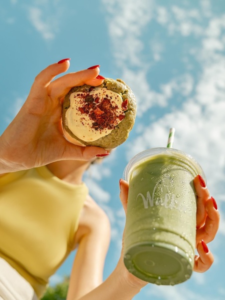 A close-up, low-angle perspective of a handheld matcha cookie paired with an iced matcha latte against a bright, sunny sky.