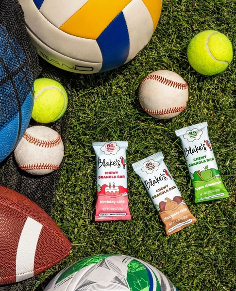 A flat-lay product hero shot of granola bars arranged on a grassy field surrounded by various sports balls to imply a healthy, active lifestyle.