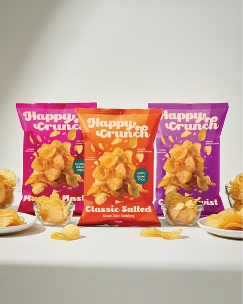 A vibrant studio shot featuring three varieties of Happy Crunch potato chips displayed in minimalist bowls against a clean, neutral background.