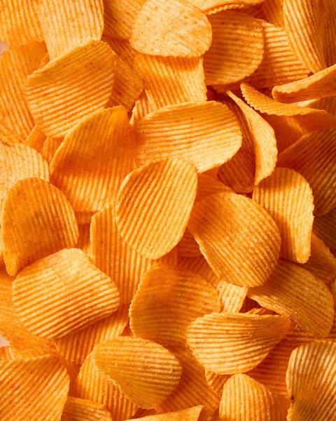 A close-up, high-detail macro shot of a pile of ridged potato chips featuring warm, golden-orange tones to emphasize crispness.