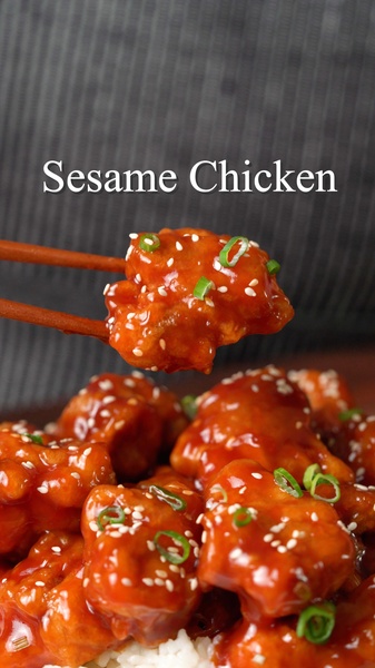 A 9:16 vertical close-up shot showcasing a piece of glistening Sesame Chicken held by chopsticks above a main dish, emphasizing texture and appetite appeal.