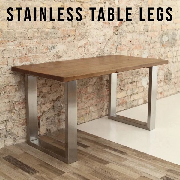A clean, square-format ad creative featuring a wood-topped desk with modern stainless steel U-shaped legs against a textured brick background.
