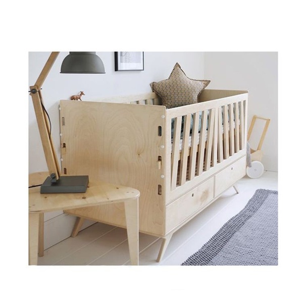 A high-quality, static image of a modern wooden crib in a bright, minimalist bedroom setting, emphasizing product craftsmanship through natural lighting.