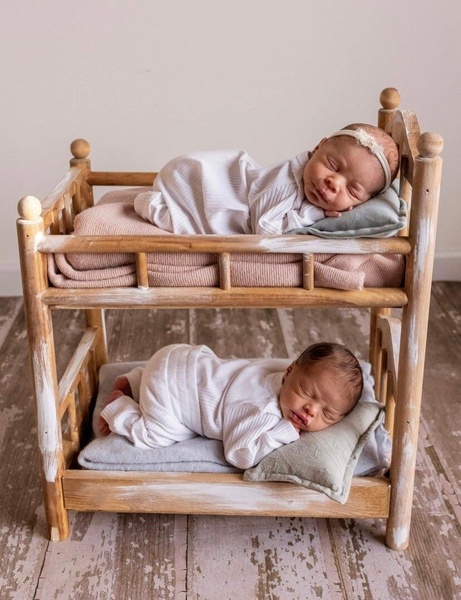 A high-quality, professional photography ad featuring a wooden bunk bed with two infants, utilizing a soft-focus, natural aesthetic to drive desire.