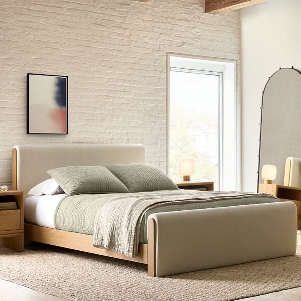 A high-end, aspirational photography shot featuring an upholstered bed in a light-filled, textured bedroom setting.