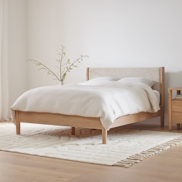 A high-end, clean-focused shot of an upholstered bed frame in a light-filled, airy room, emphasizing a calm and serene aesthetic.